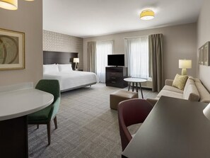 Habitación de hotel con cama, escritorio con silla, sofá, televisor y lámpara.