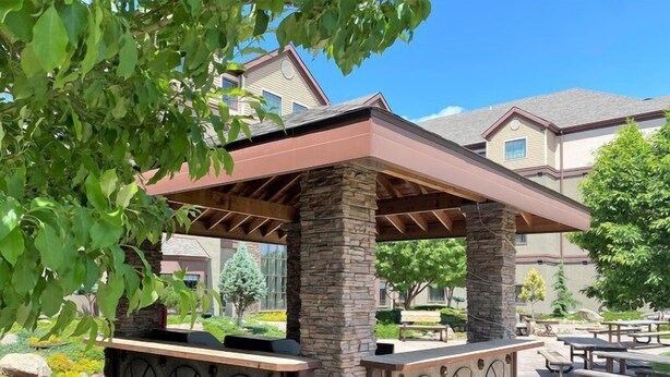 A covered outdoor seating area with stone pillars and a metal grill.