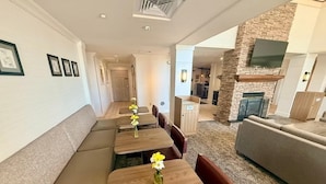 Un intérieur moderne avec une longue table à manger, des sièges rembourrés, un mur d’accent en pierre et un téléviseur à écran plat.