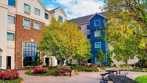 A courtyard with outdoor seating, a building with a stone facade, and a blue building with multiple windows.