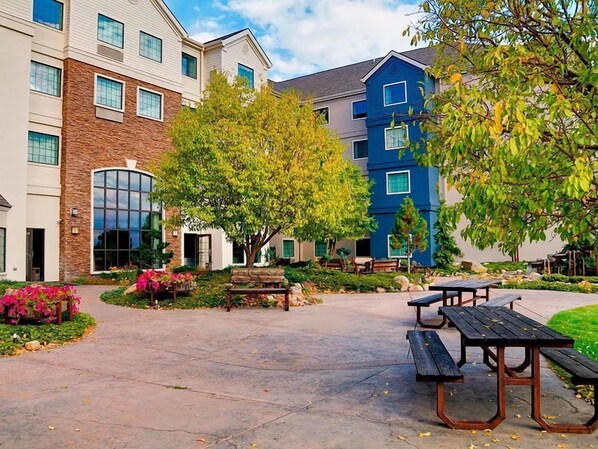 A courtyard with outdoor seating, a building with a stone facade, and a blue building with multiple windows.