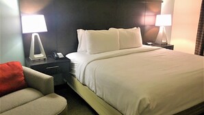 Een hotelkamer met een bed, twee nachtkastjes met lampen, een stoel en een nachtkastje met een telefoon.