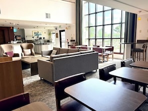 Un hall d’hôtel moderne avec un espace salon, une cuisine à l’arrière-plan et de grandes fenêtres.