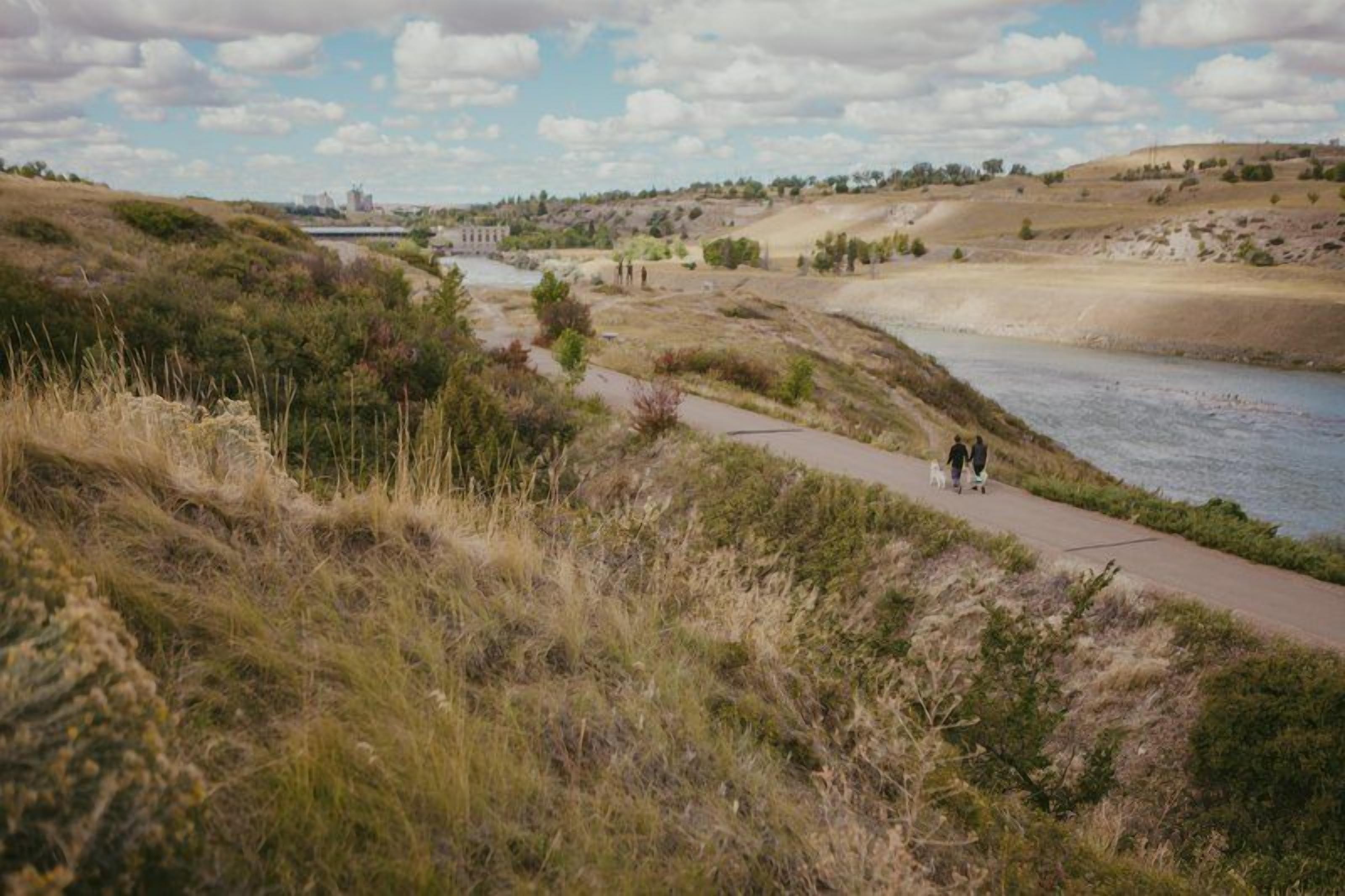 A riverside path with grassy banks and a distant building.