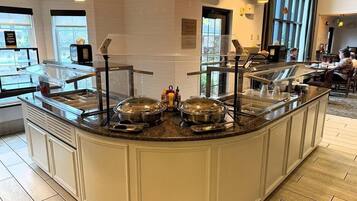 A buffet area with a curved counter, stainless steel serving dishes, and overhead yellow pendant lighting.