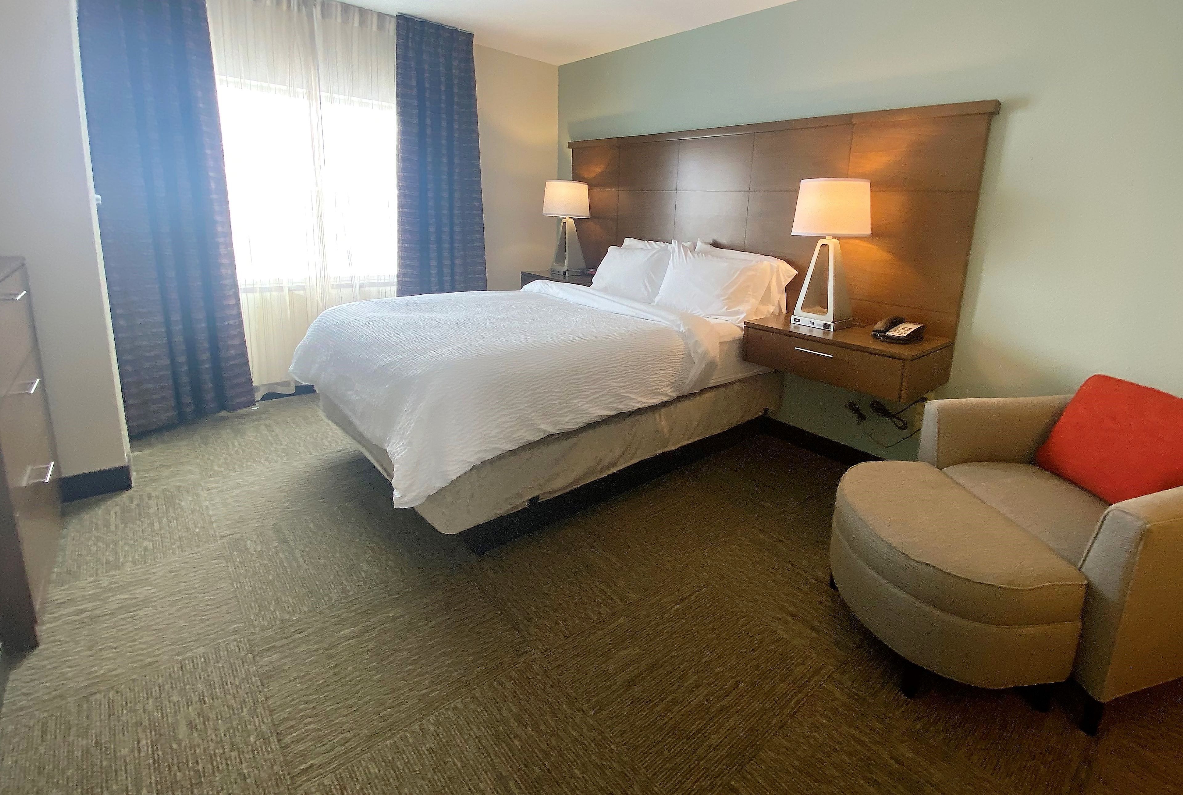 A hotel room with a bed, two bedside lamps, a chair, and a nightstand with a phone.