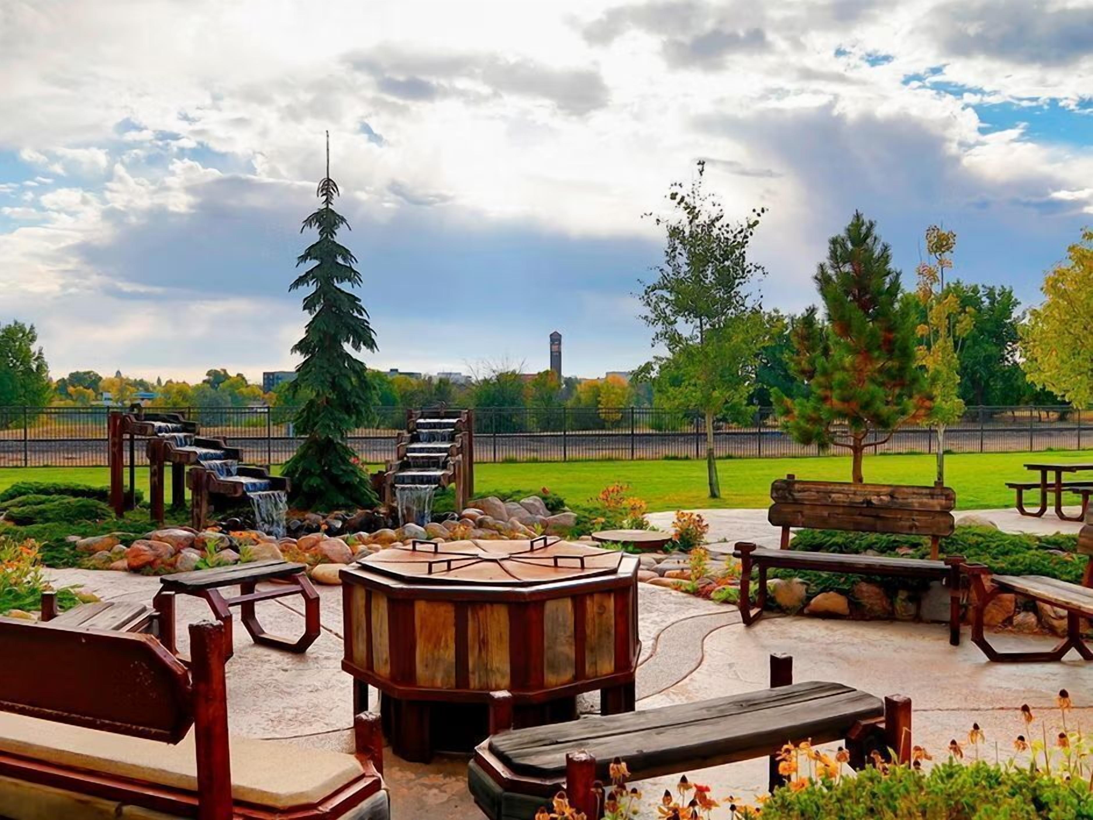 A park with wooden benches, a wooden gazebo, and a tall evergreen tree.