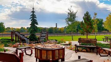 A park with wooden benches, a wooden gazebo, and a tall evergreen tree.