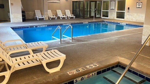 An indoor swimming pool with lounge chairs, a pool ladder, and a sign indicating a depth of 6 feet. - Missouri River View Suite | Free Breakfast! (Great Falls)