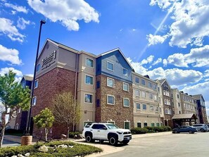 A multi-story hotel with a stone facade, a parking lot, and a clear blue sky.