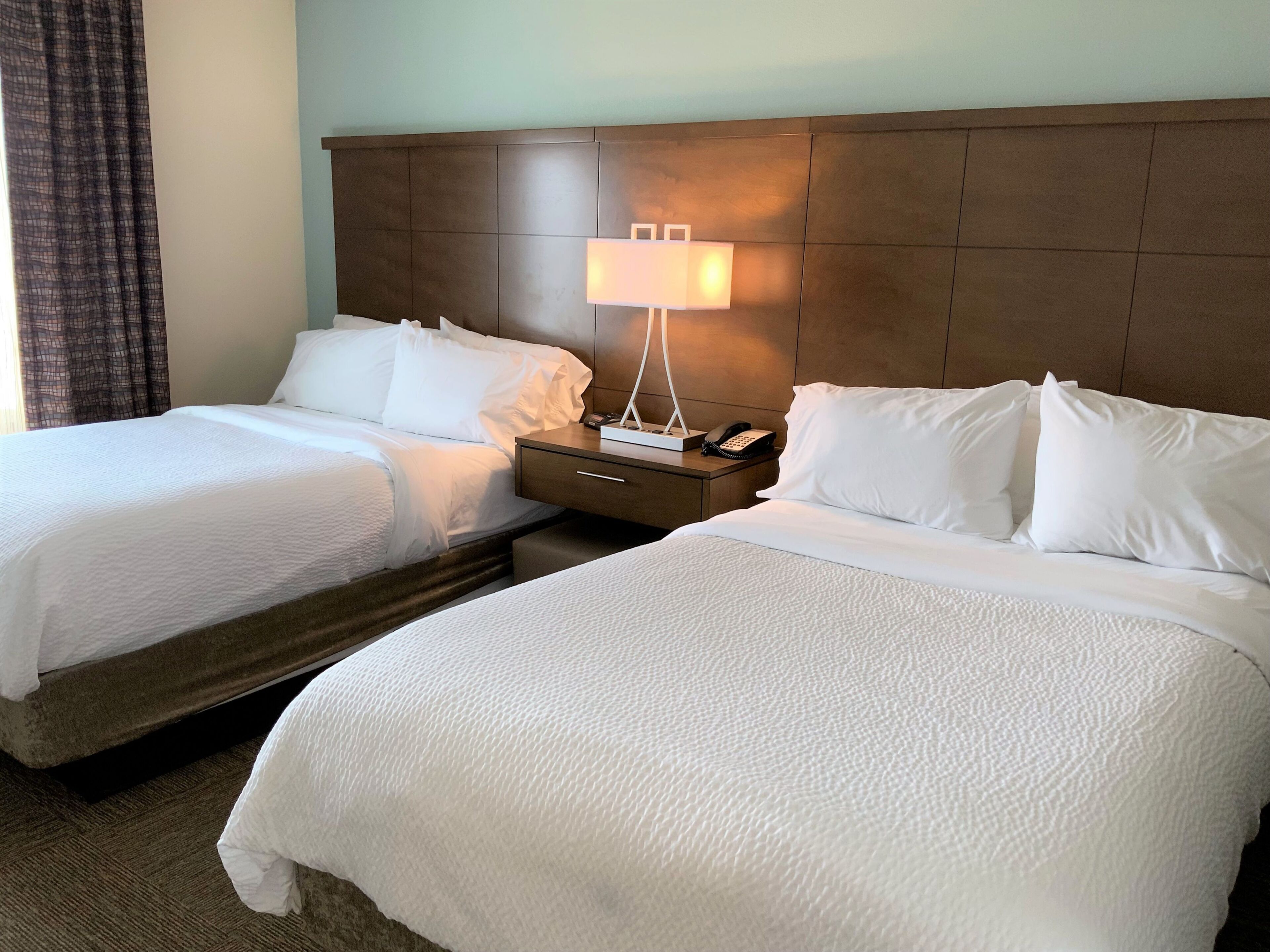 A hotel room with two beds, a nightstand with a lamp, and a telephone.