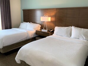 A hotel room with two beds, a nightstand with a lamp, and a telephone.