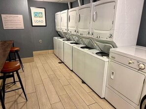 A laundry facility with multiple washing machines and dryers, a sign indicating free guest laundry, and a bar stool.