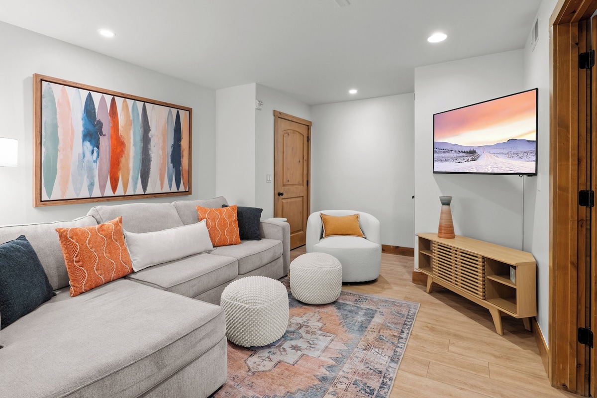 Una sala de estar moderna con un sofá, otomanas, un televisor y un cuadro en la pared.