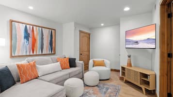 A modern living room with a sofa, ottomans, a TV, and a painting on the wall.