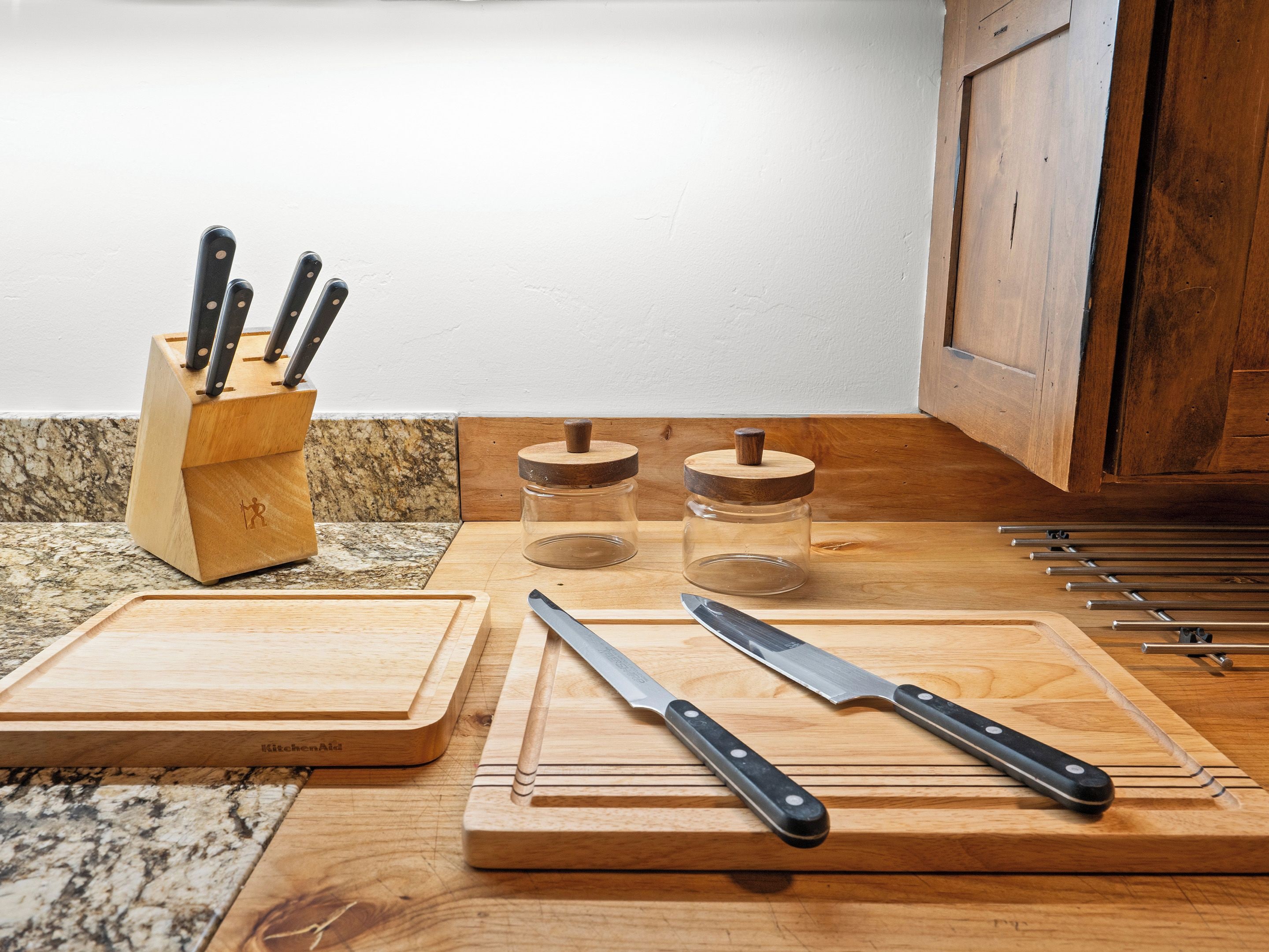 A kitchen counter with wooden cutting boards, two knives, and two glass jars with wooden lids.