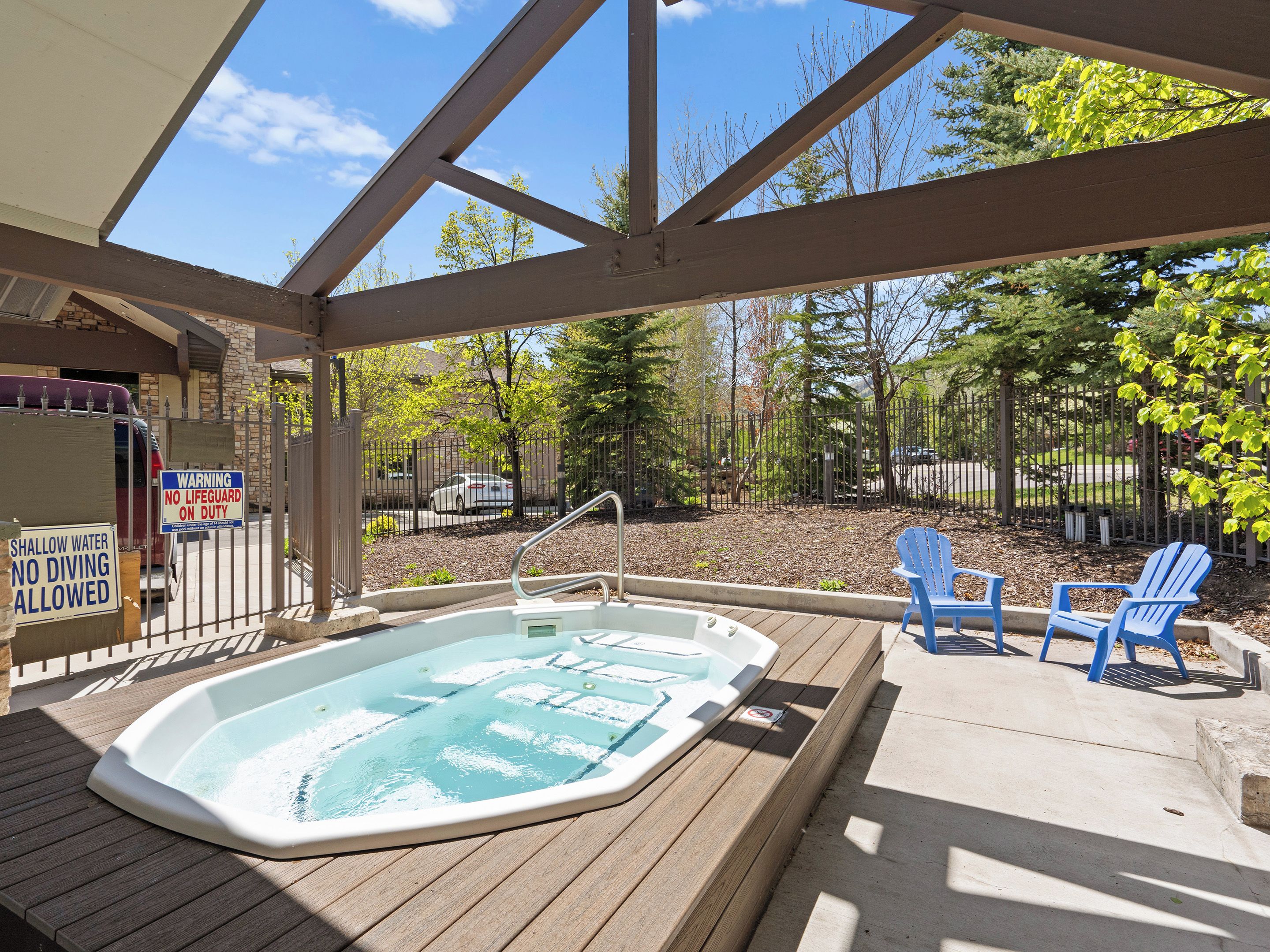 Un jacuzzi en un área exterior techada con vista a un patio cercado y árboles.