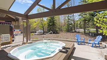 Un jacuzzi en un área exterior techada con vista a un patio cercado y árboles.