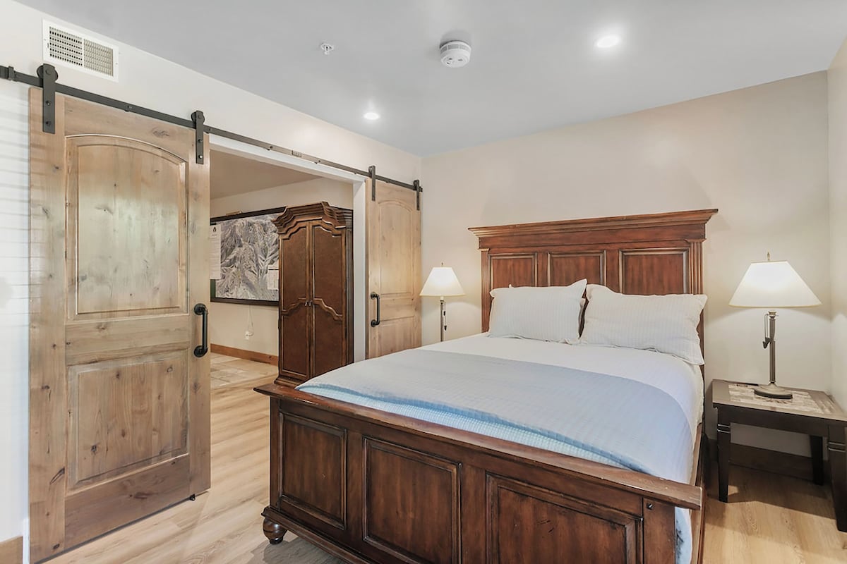 Un dormitorio con una cama de madera, dos lámparas de noche, una mesita de noche y una puerta corredera que da a otra habitación.