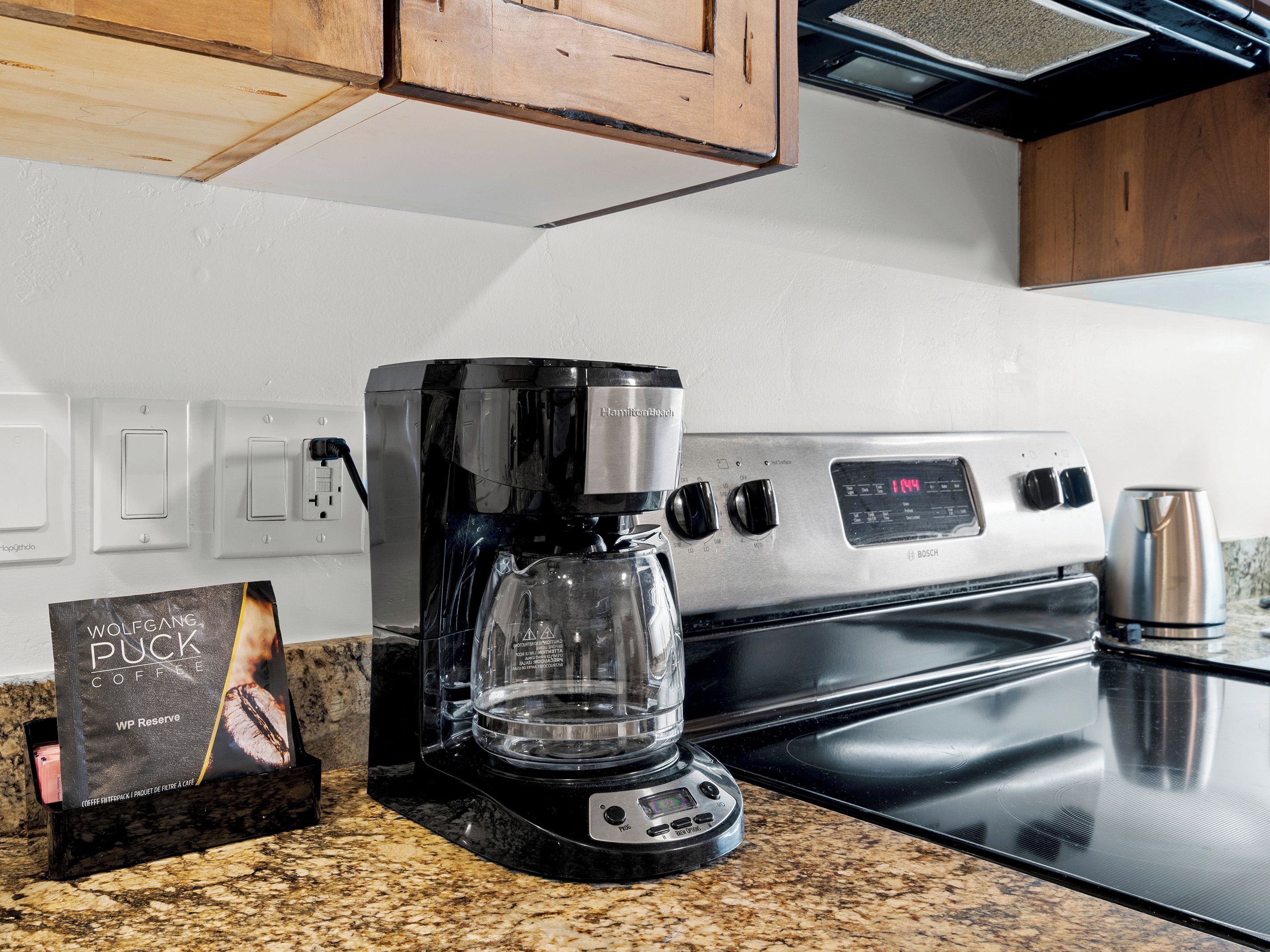 A kitchen with a Bosch coffee maker, a coffee pod box, and a stainless steel kettle on the counter.