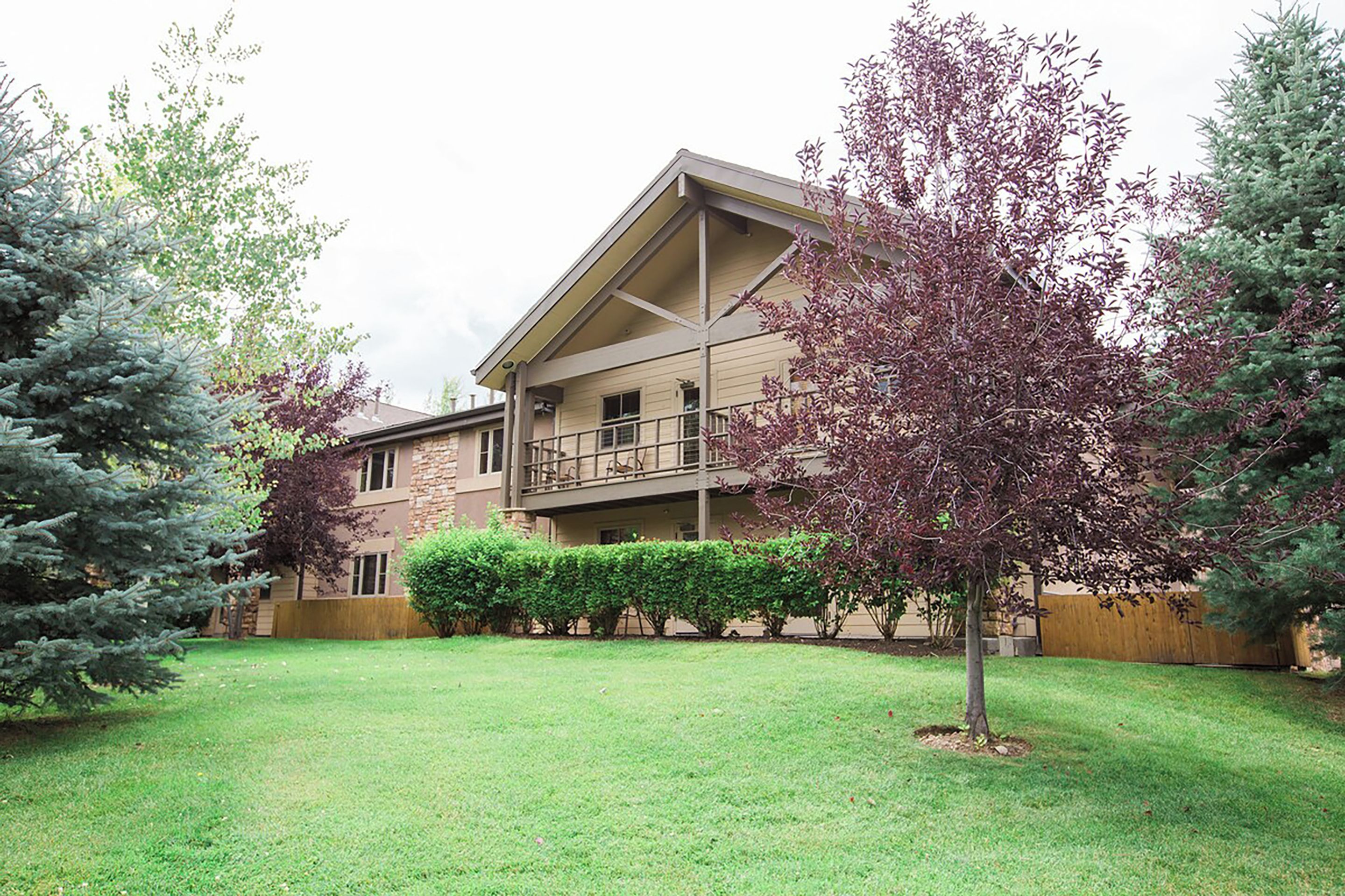 A multi-story building with a flat roof, a balcony on the second floor, and a well-maintained lawn with trimmed bushes and trees.