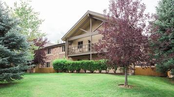 A multi-story building with a flat roof, a balcony on the second floor, and a well-maintained lawn with trimmed bushes and trees.