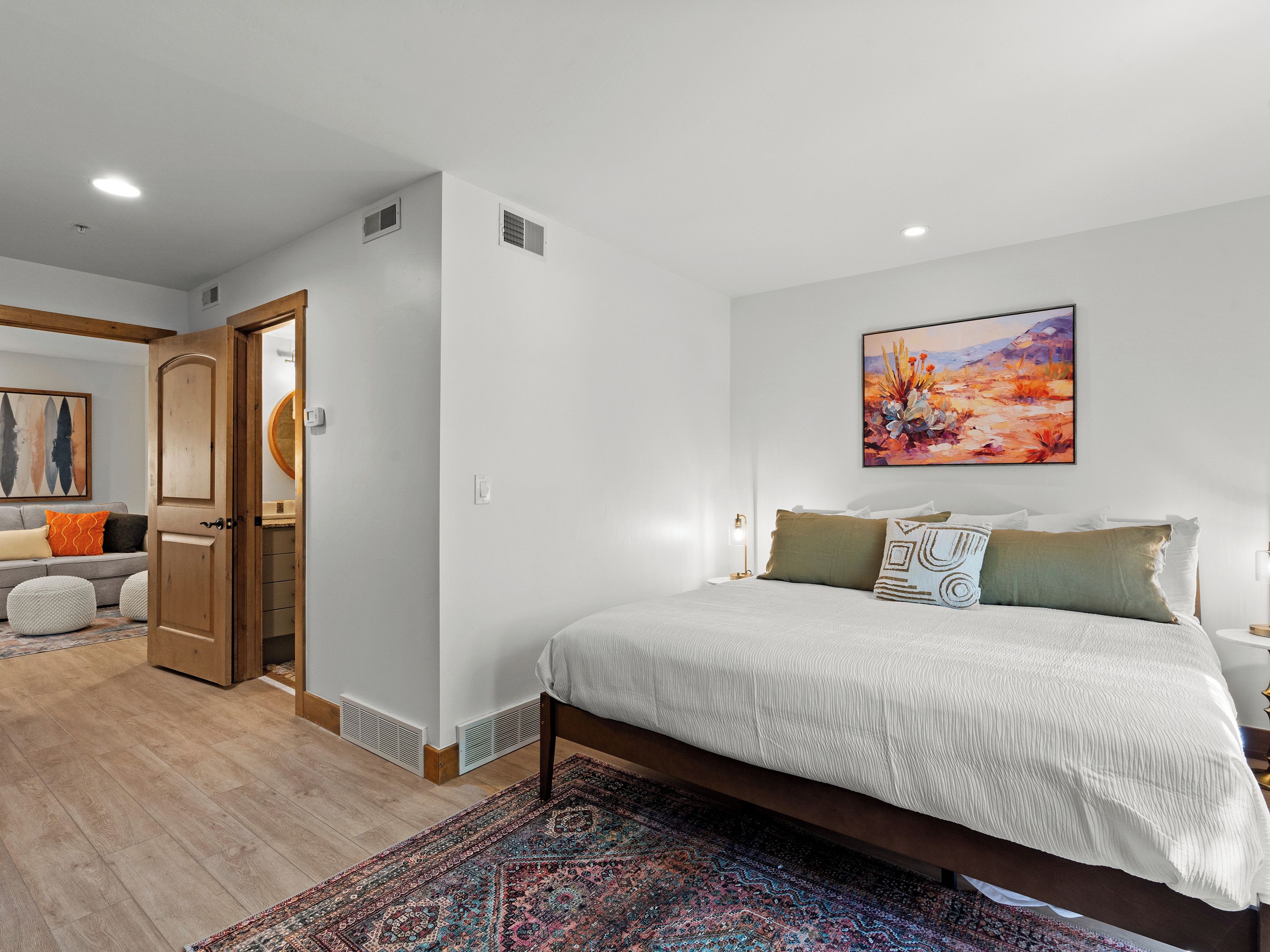 A bedroom with a bed, a nightstand, a painting, and a door leading to another room.
