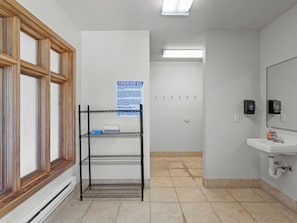 Un baño con lavamanos blanco, un espejo, estante con normas de higiene y una ventana con persianas.