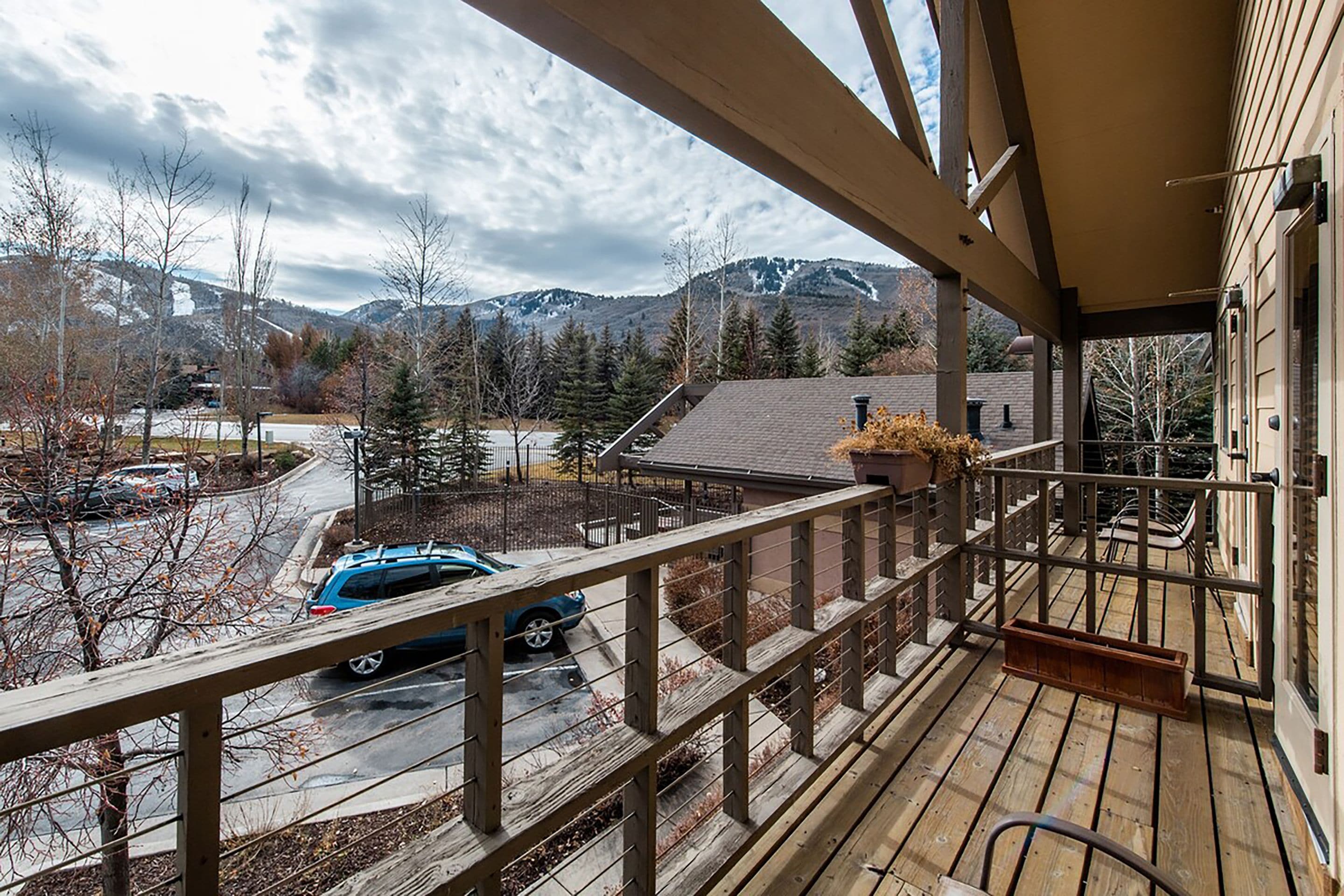 A wooden deck with a view of a parking area and mountains in the background.