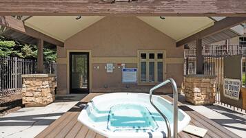 A hot tub under a wooden pergola with a stone wall and a metal fence.