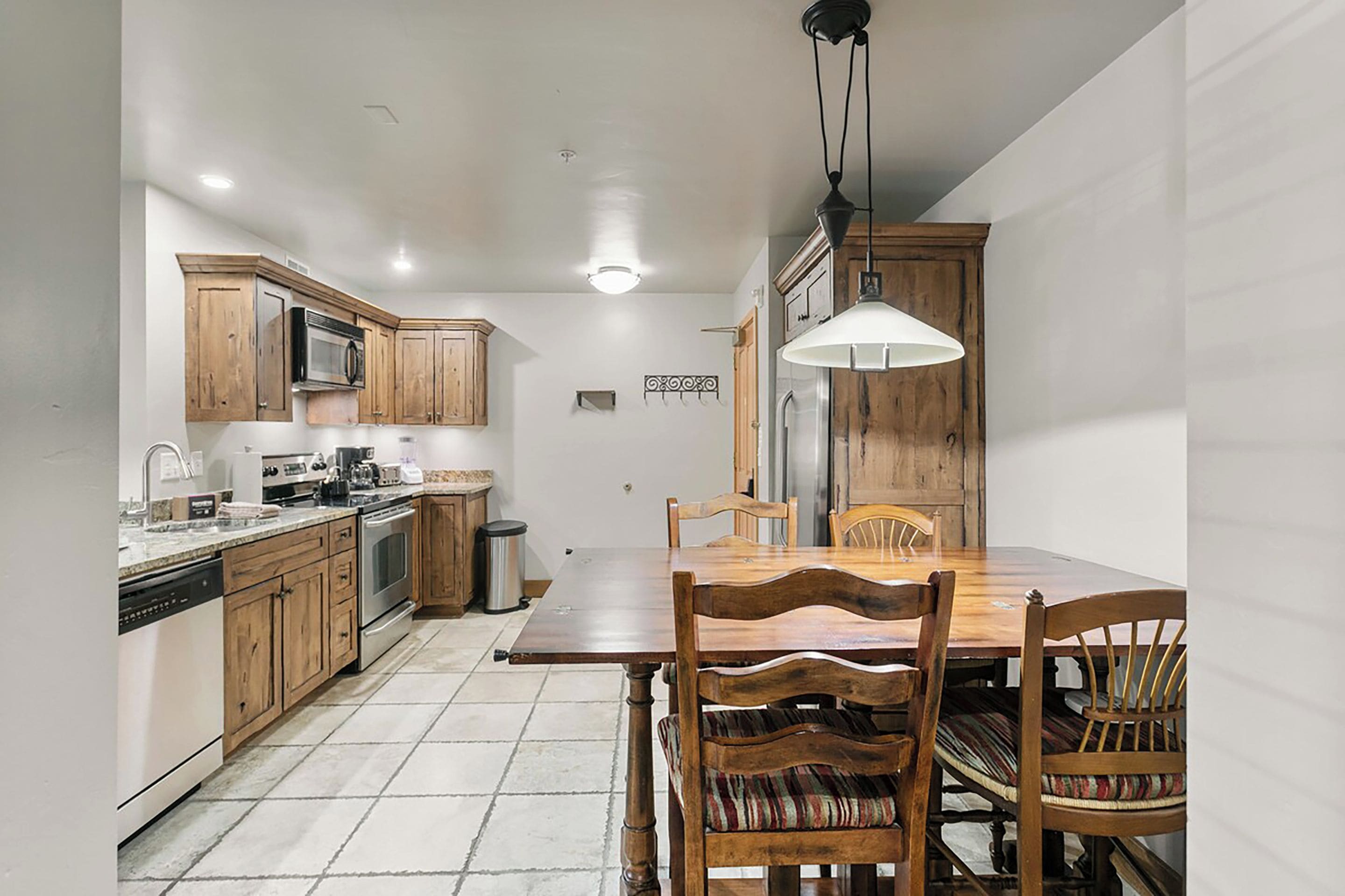 A compact kitchen with wooden cabinets, a stainless steel refrigerator, and a dining table with chairs.