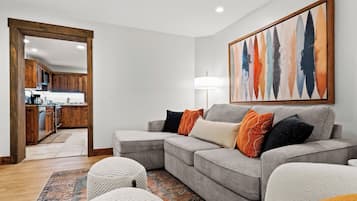 A modern living room with a grey sectional sofa, white poufs, and a colorful abstract painting.