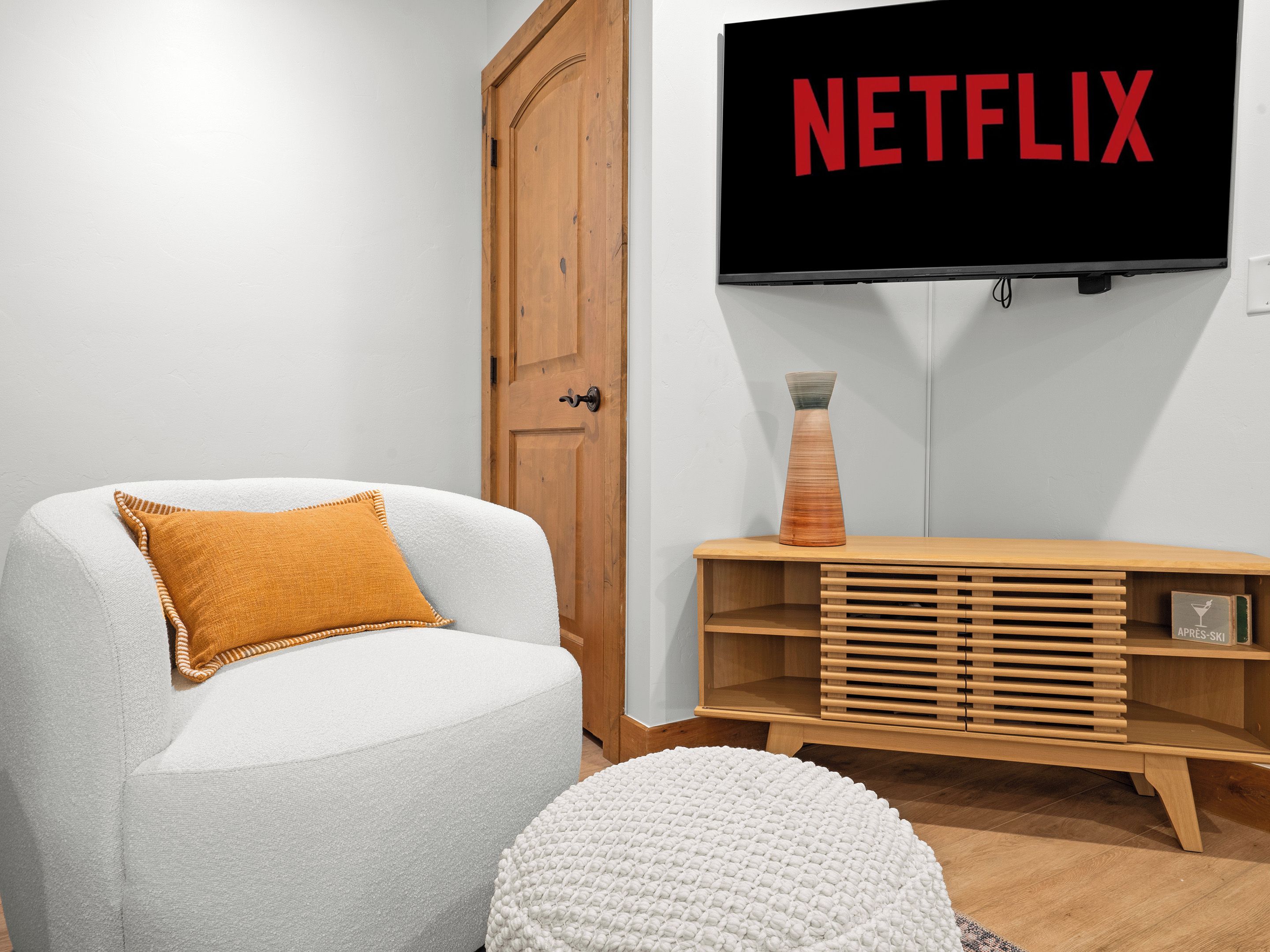 Ein Wohnzimmer mit einem weißen Sessel, einem Holztisch und einem Fernseher, der 'NETFLIX' anzeigt.