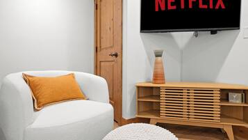 Ein Wohnzimmer mit einem weißen Sessel, einem Holztisch und einem Fernseher, der 'NETFLIX' anzeigt.
