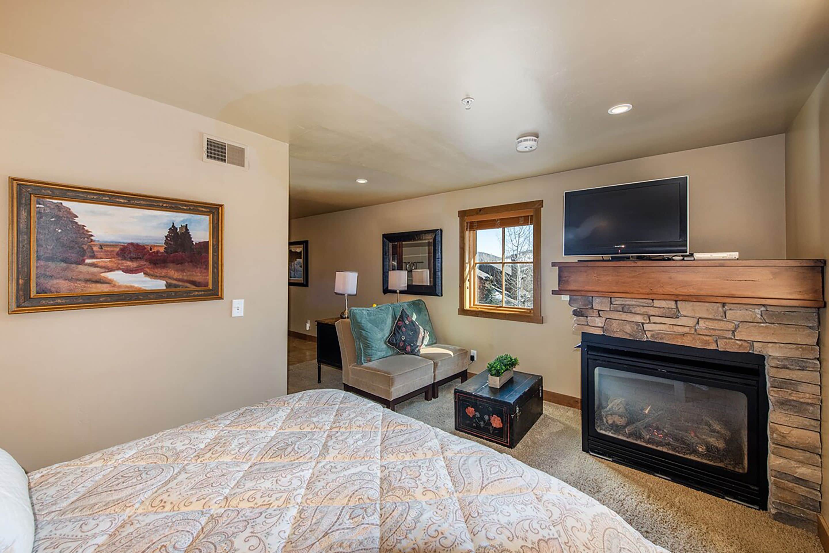 A bedroom with a bed, a fireplace, a television, and a painting on the wall.