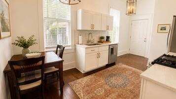 A kitchen with white cabinets, a wooden dining table, a rug, and pendant lighting.