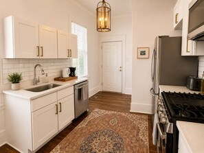 A kitchen with white cabinets, stainless steel appliances, a wooden countertop, and a patterned rug.