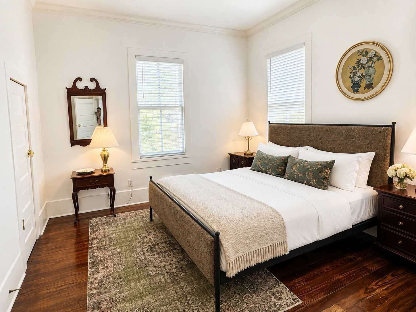 A bedroom with a bed, bedside tables, a mirror, and a window.