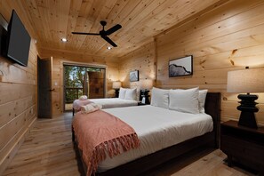 Un dormitorio de cabaña de madera con dos camas, un ventilador de techo y un televisor montado en la pared.