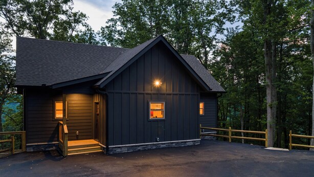 A dark wooden cabin with a sloped roof, a front porch, and a stone foundation. - NEW CABIN: Sauna | Hot Tub | Fire Pit | EV (Gatlinburg)