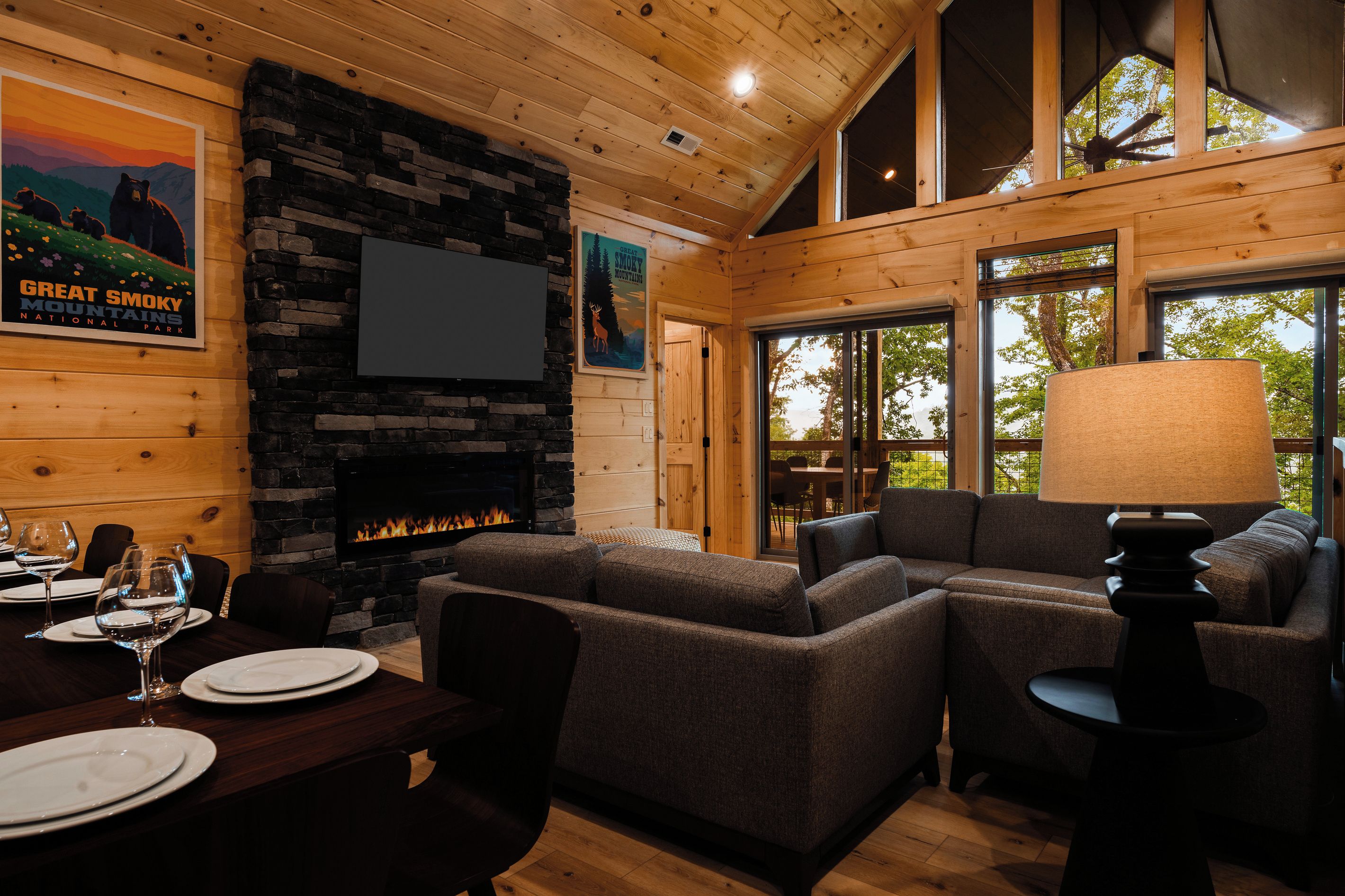 A cozy interior with a stone fireplace, wooden walls, and large windows.