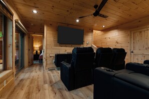 Ein gemütliches Holzinterieur mit einem an der Wand befestigten Flachbildfernseher, einem Deckenventilator und einer Sitzecke mit schwarzen Ledersofas.