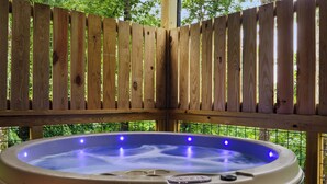 A hot tub with a wooden fence enclosure, surrounded by greenery. - NEW CABIN: Sauna | Hot Tub | Fire Pit | EV (Gatlinburg)