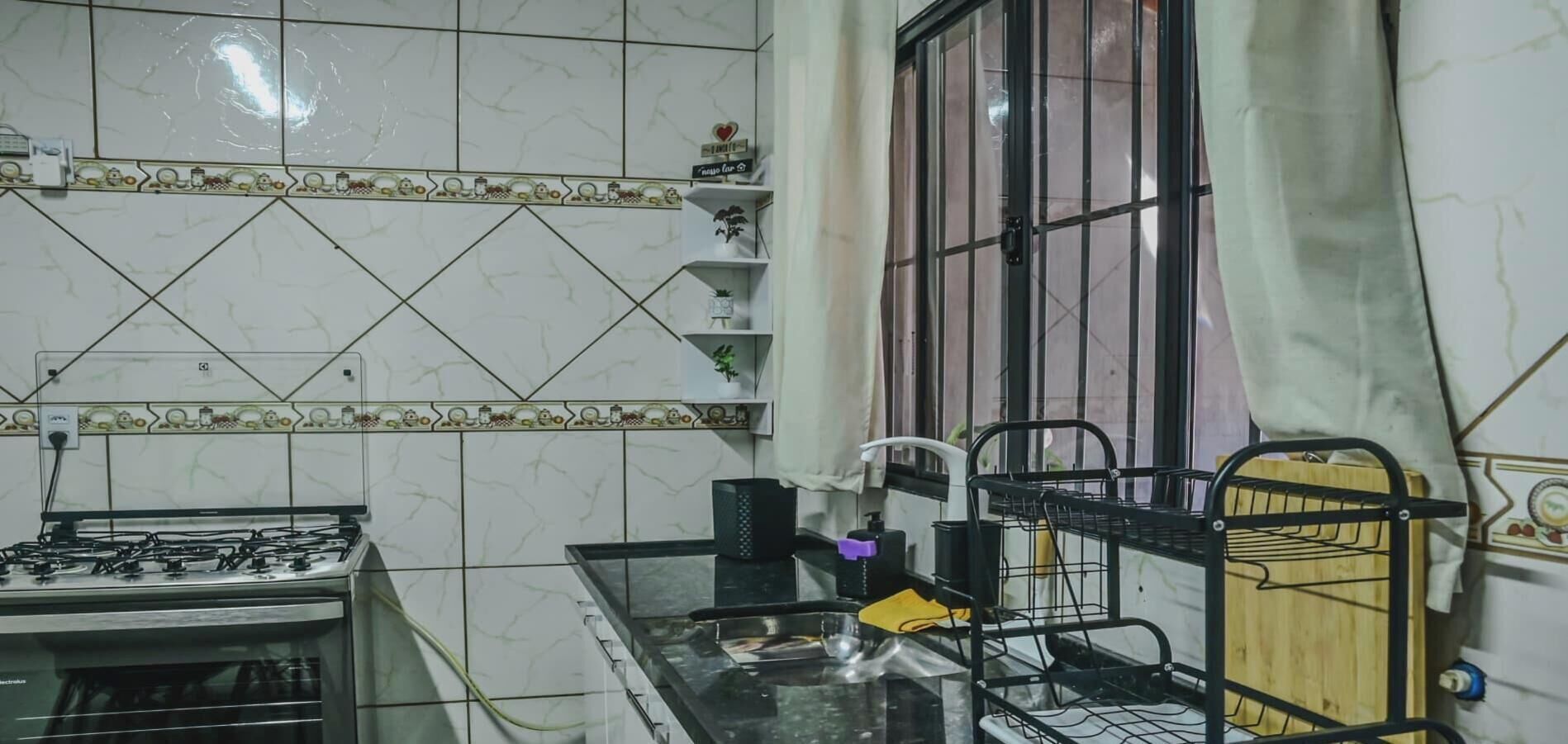 A kitchen with a gas stove, a sink, a metal rack, and a window with curtains.