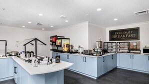 A breakfast bar with a sign offering free daily breakfast, a coffee machine, and various food items.