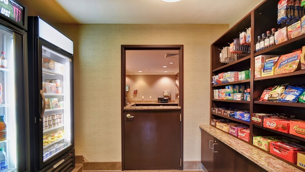 A hotel pantry with a refrigerator stocked with beverages, a microwave, and shelves with snacks and condiments.
