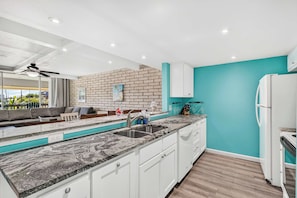 A modern kitchen with a marble countertop, white cabinets, and a teal accent wall. - Jade’s Getaway | 2BR Condo Near the Beach with Pool & Private Boardwalk (Port Aransas)