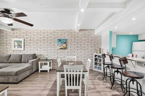 Ein modernes Wohnzimmer mit Backsteinwand, einer Couch, einem Esstisch mit Stühlen und einer Küchenzeile mit Barhocker.