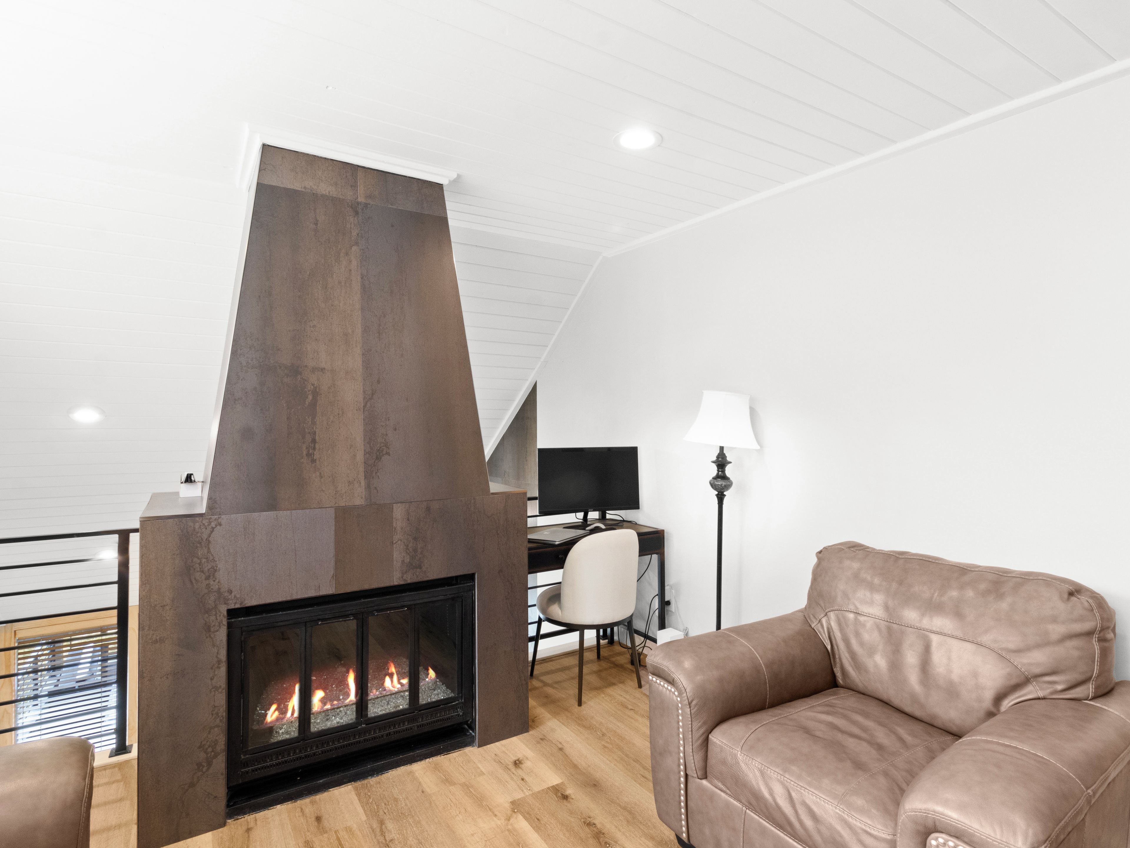 A modern living room with a fireplace, leather sofa, and a desk with a computer.