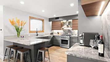 A modern kitchen with a central island, bar stools, a built-in oven, and a wine bottle.